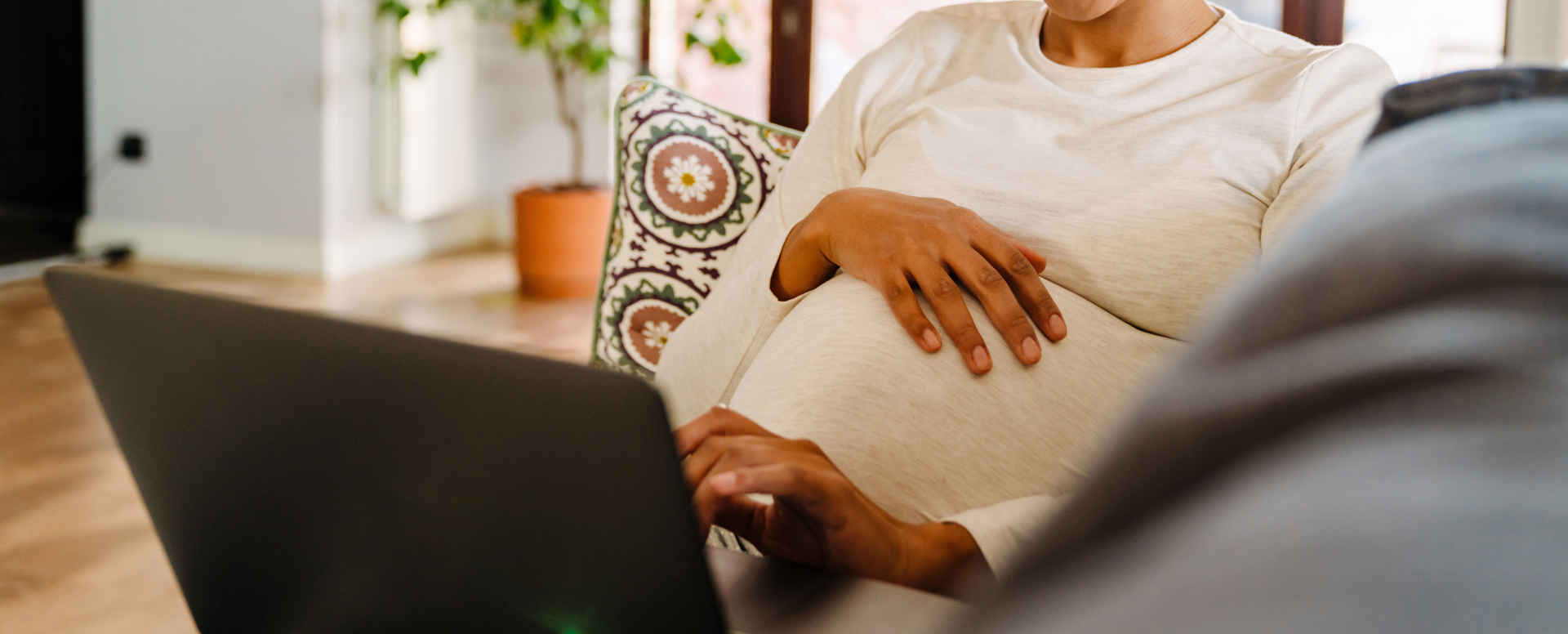 Gravid kvinna med laptop i soffa